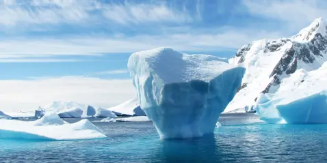 Large iceberg floating in the ocean with snow-covered mountains in the background