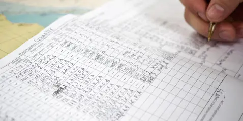 Close-up of a hand writing on a detailed logbook with various entries.