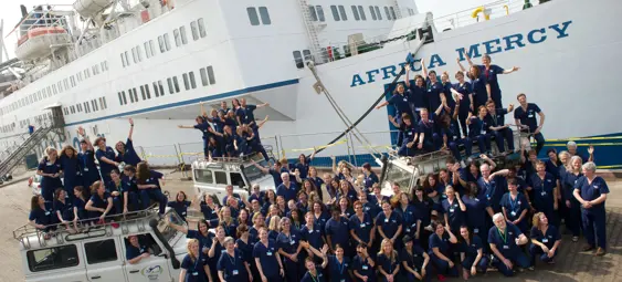Besætningen på Africa Mercy-skibet poserer foran skibet i deres blå uniformer