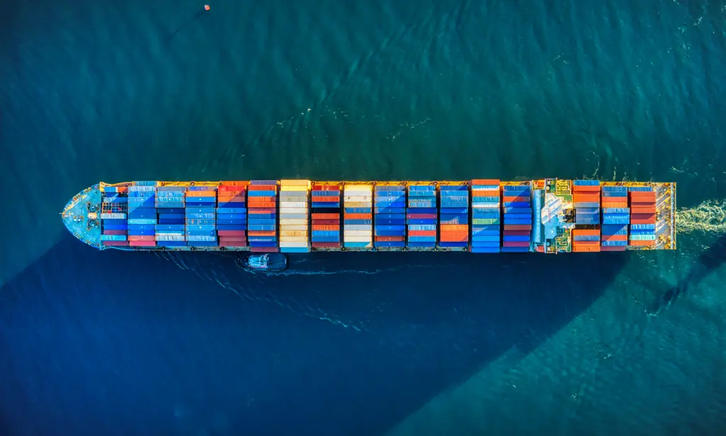 A container ship at sea viewed from above, featuring multicolored cargo containers on its deck.