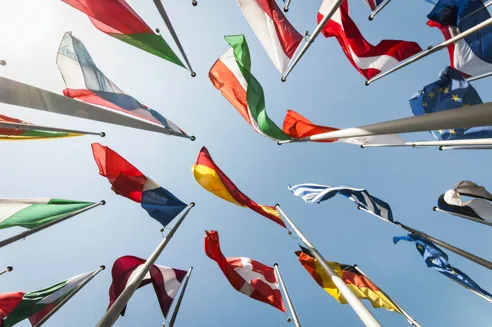Multiple national flags waving against a clear blue sky