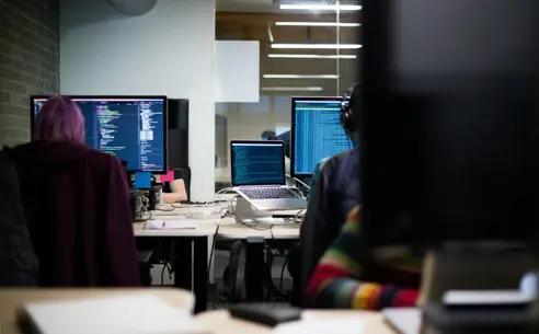 Two people working on computers in an office, seen from behind