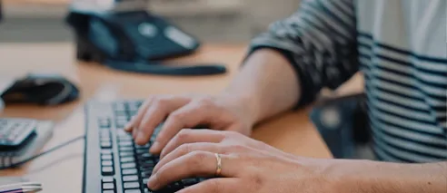 Close-up of hands typing on a keyboard in an office setting