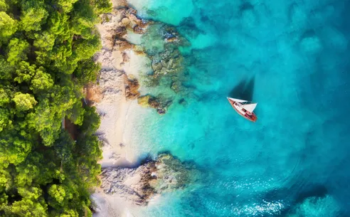 En luftfoto af en båd på stranden, omgivet af sand og klart blåt vand i Kroatien