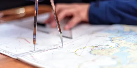 Person planning navigation with divider on nautical paper chart