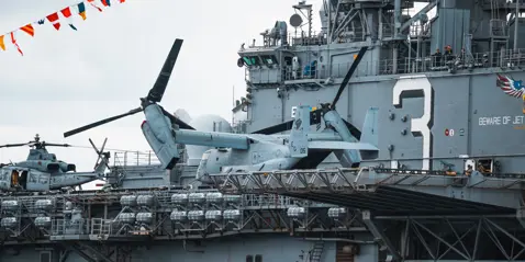 Military helicopters on the deck of a large navy ship, with colorful flags overhead.