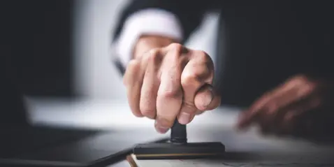 En hånd presser et stempel fast på et stykke papir