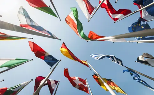 Multiple national flags waving against a clear blue sky